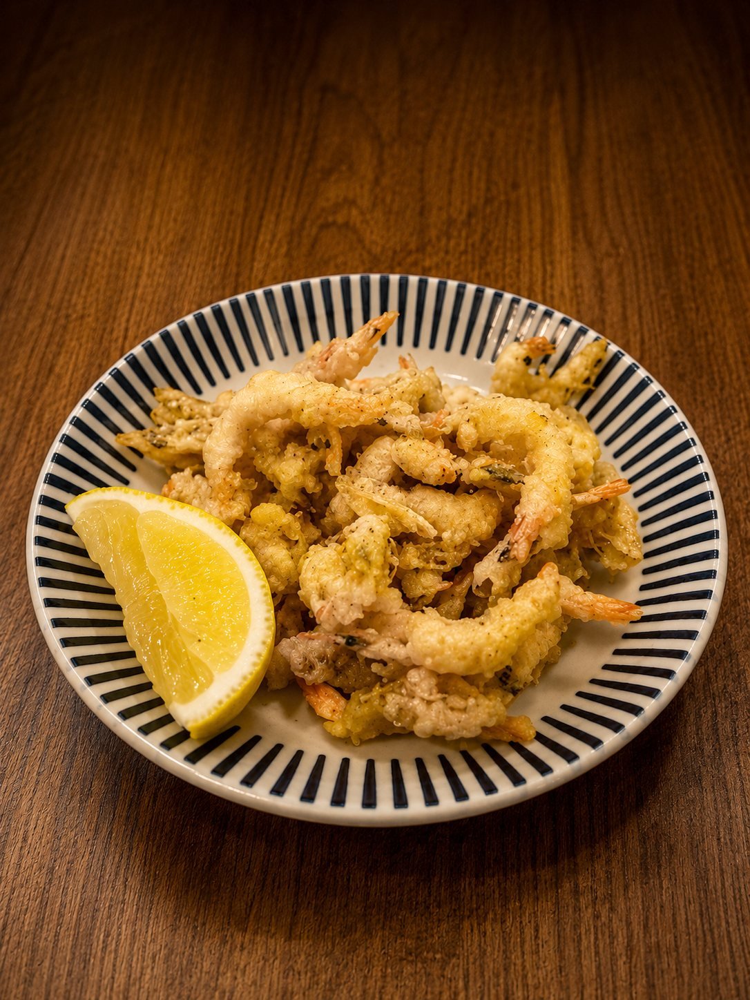 Crispy fried river prawns piled on a striped plate with a lemon wedge
