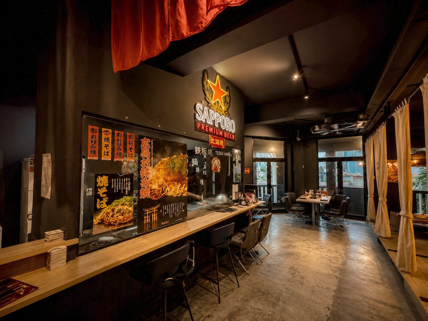 The teppan counter and dining room at Nanjya Monjya × Miseya, lit by the Sapporo neon